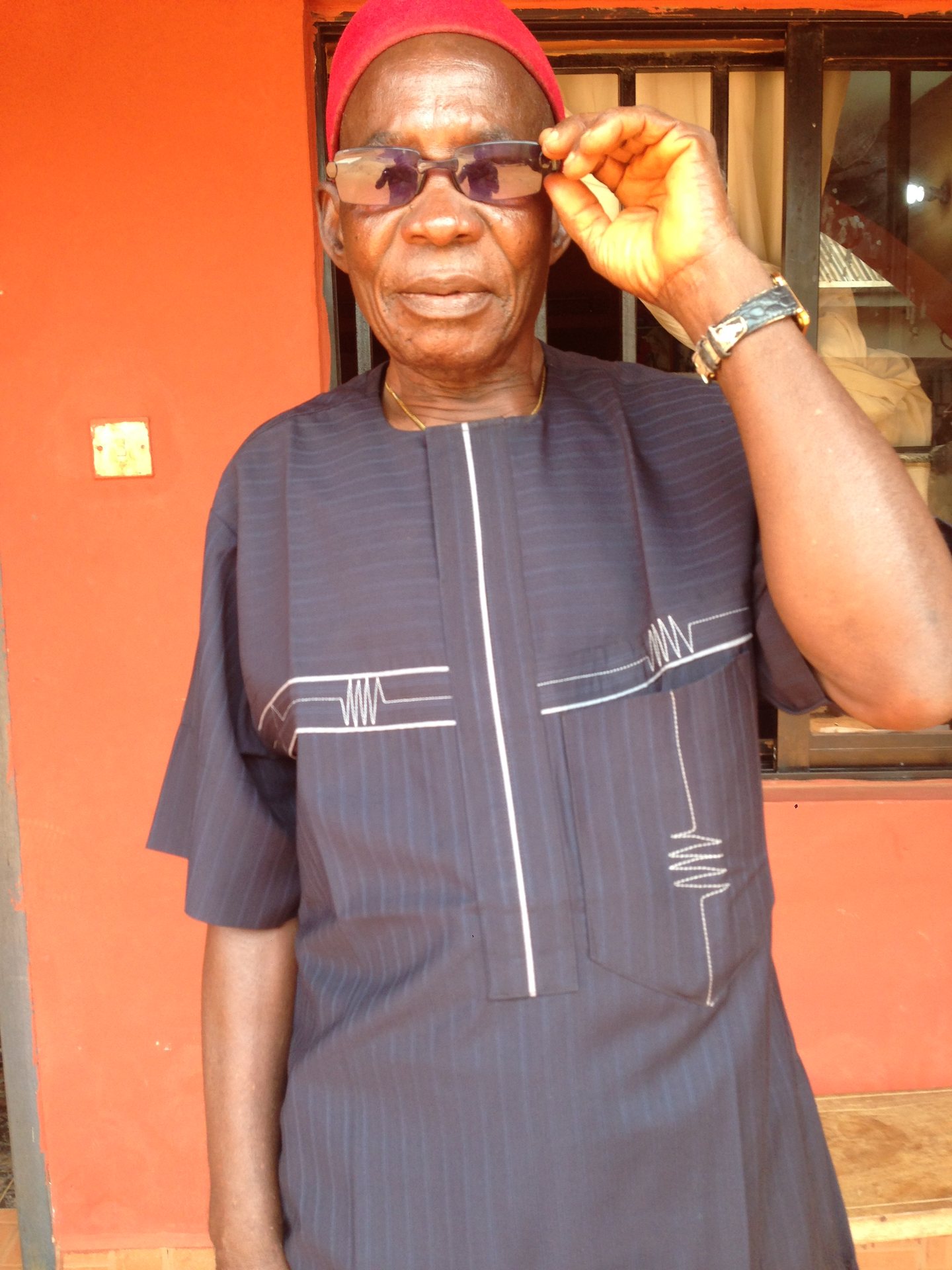 Pa. Ogunor smiling playfully, holding his glasses
